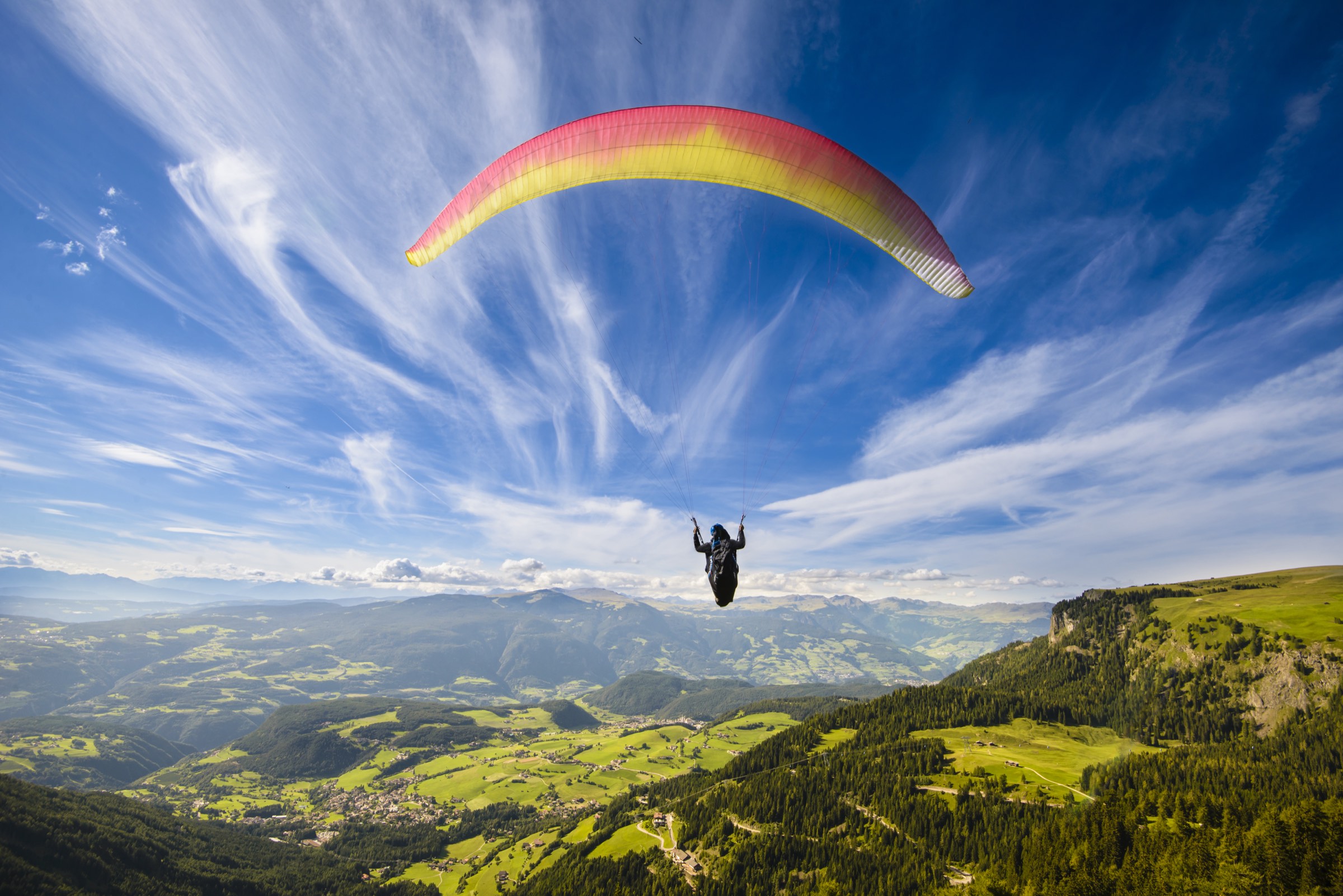 A paraglider soaring over green mountain valleys
